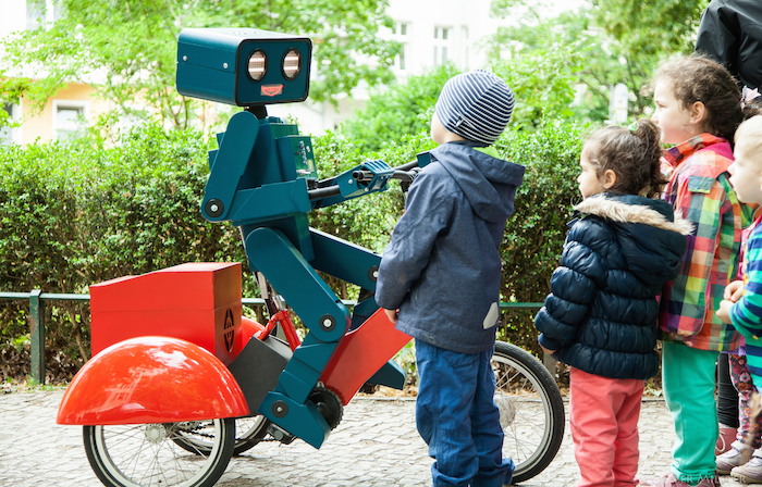 hugo der sprechende Roboter auf rotem Fahrrad mit kindern